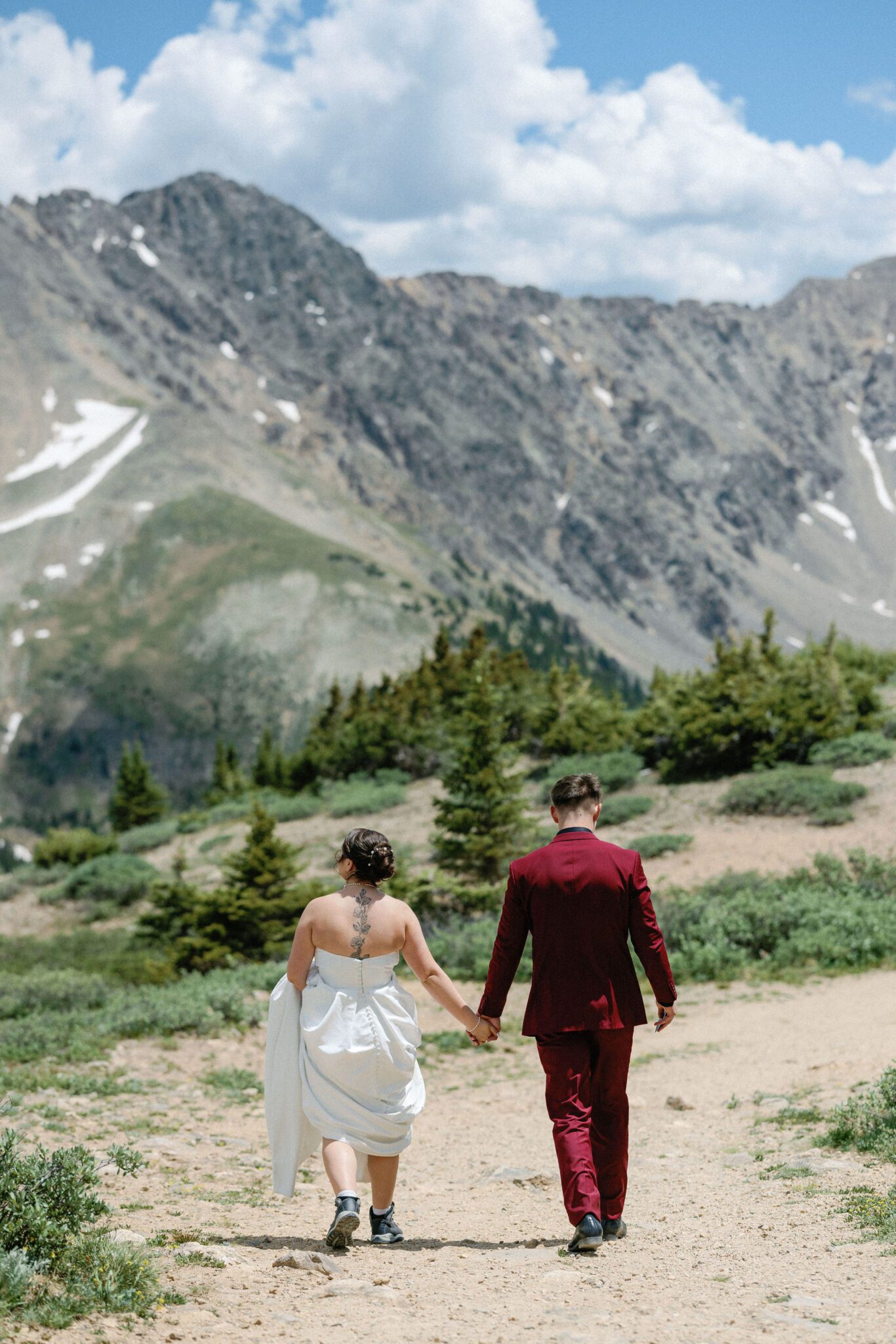 bride and groom hold hands and walk along trail during hiking wedding