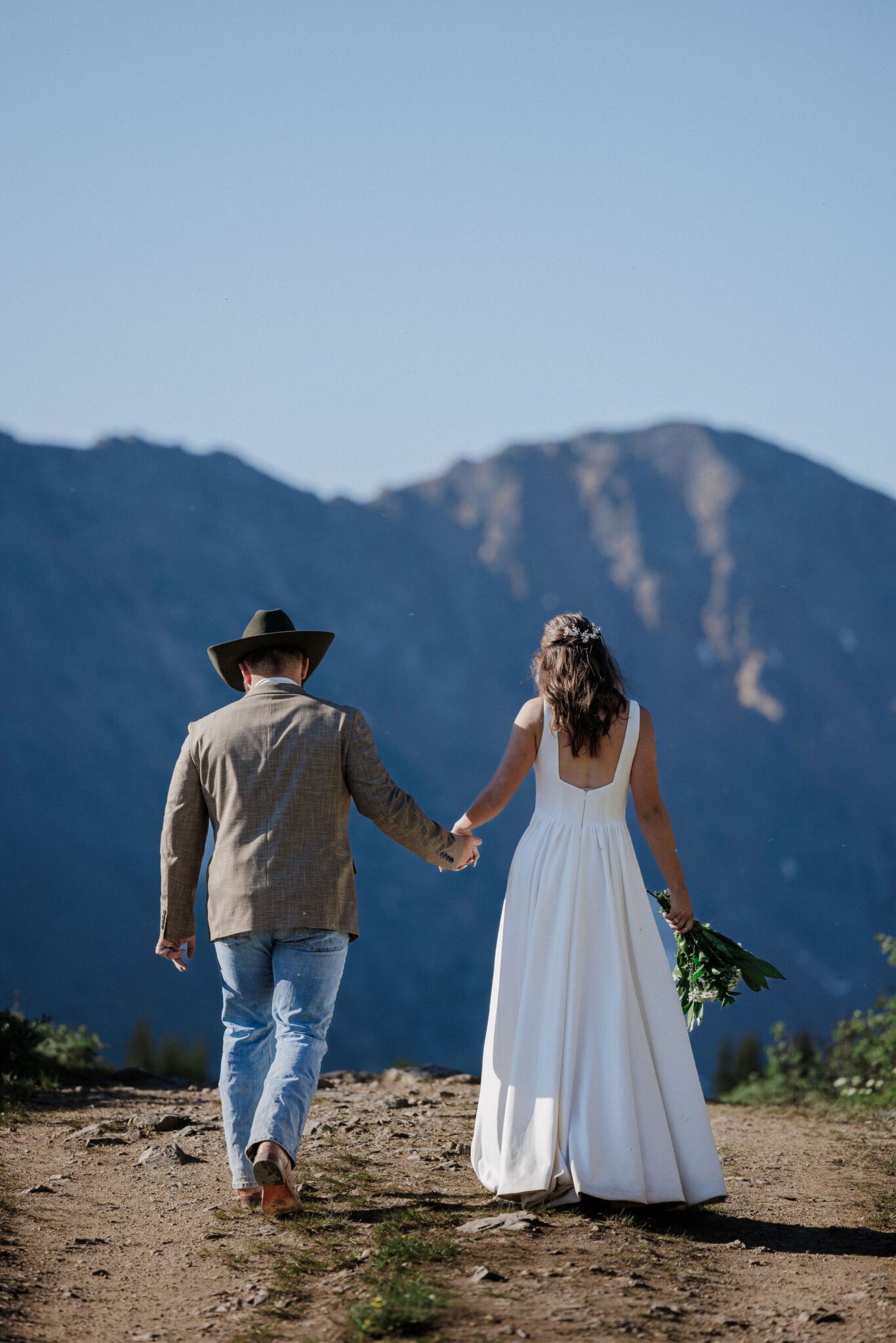 bride and groom hold hands ans they walk up a trail at loveland pass, a colorado elopement location