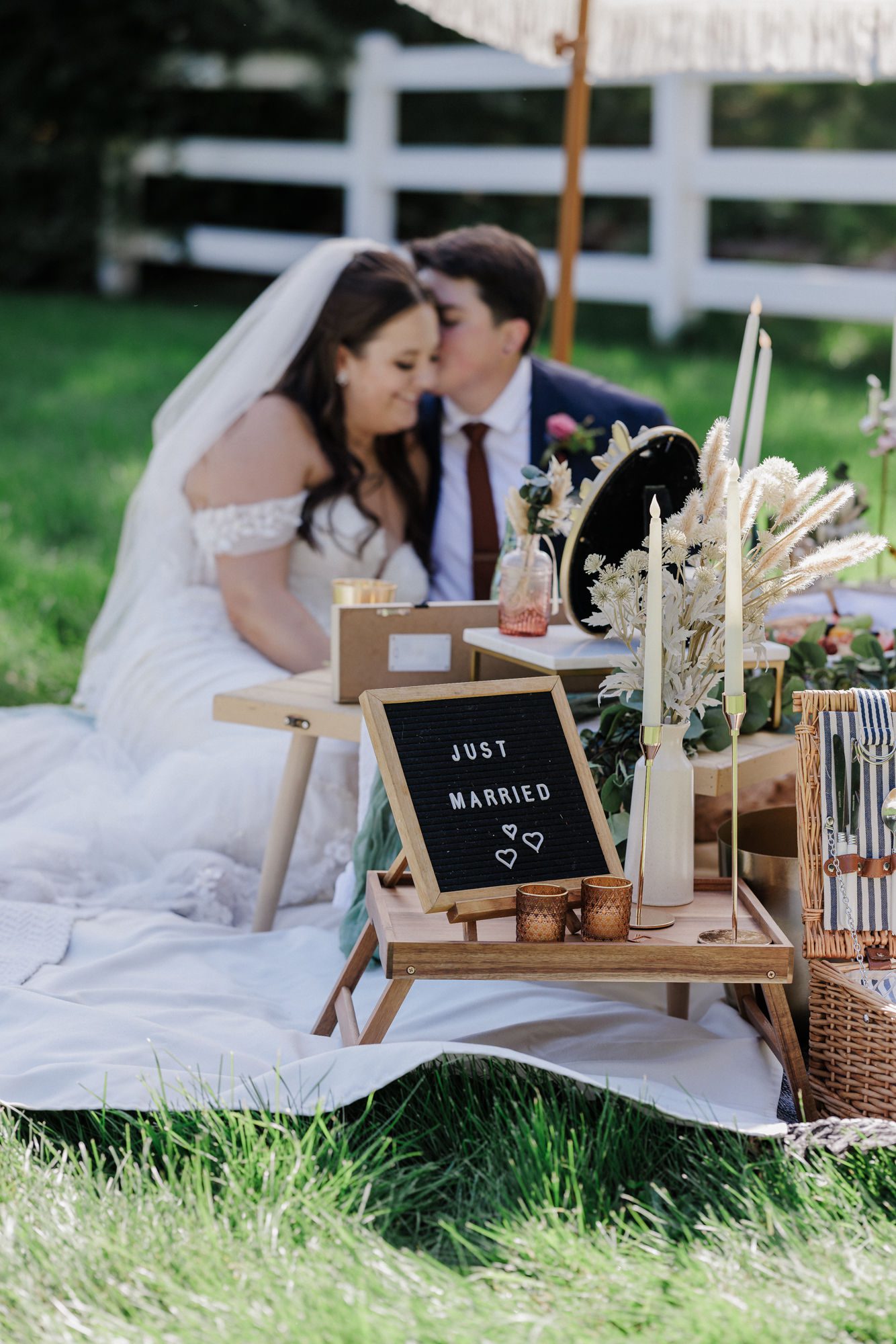 two brides sit on a blanket during their wedding picnic at a private venue