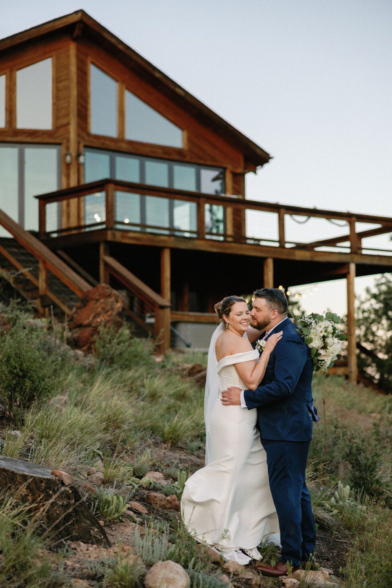 bride and groom stand down the hill from the deck of an airbnb and take wedding photos