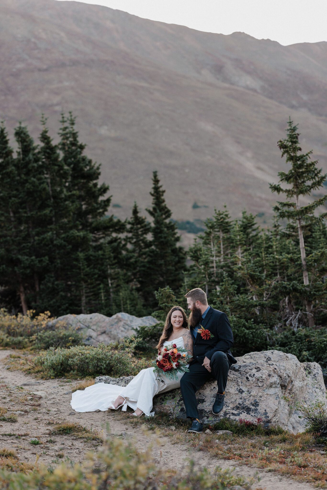 bride and groom sit on rock in the mountains during their wedding photos at loveland pass, a colorado elopement location