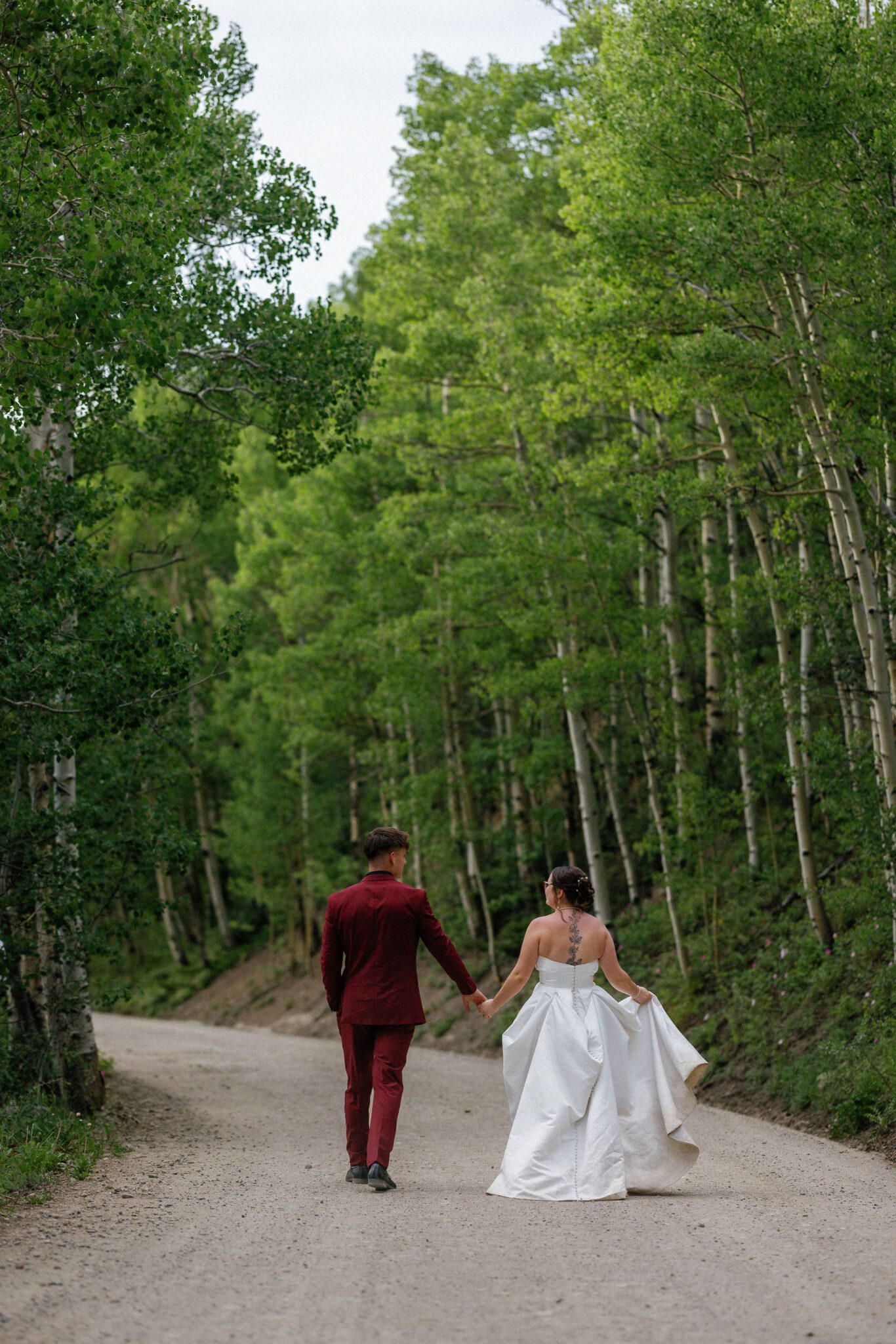 bride and groom hold hands and walk down dirt road lined with aspen trees